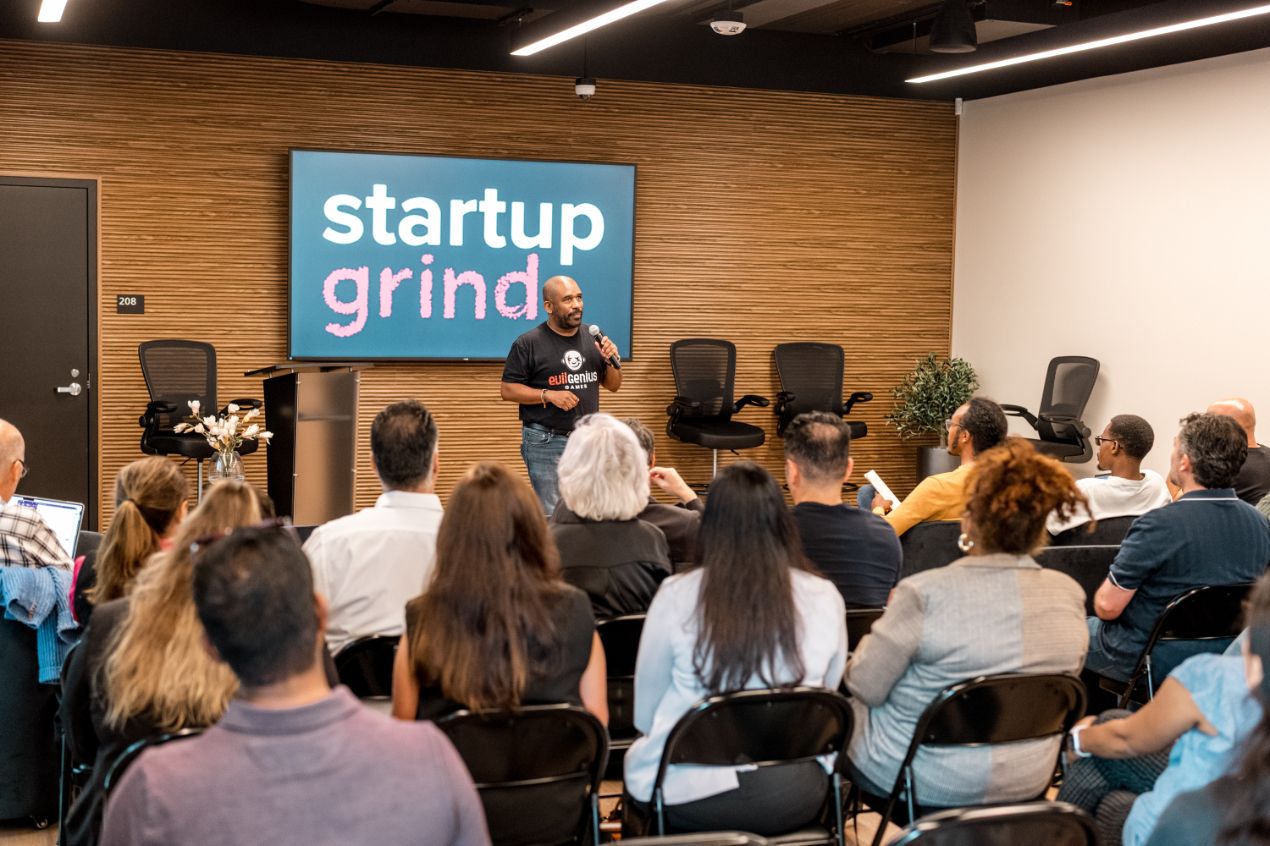 A packed room watching a founder pitch at STAK